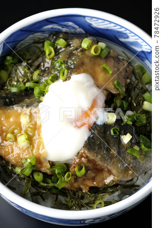 A bird's-eye view of a yellowtail teriyaki rice bowl topped with hot balls and plenty of small onions on a black background 78472926