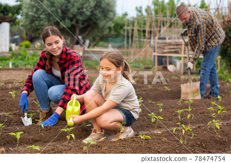 Mother and daughter watering plants at garden closeup Mother and daughter watering plants at garden closeup 78474754