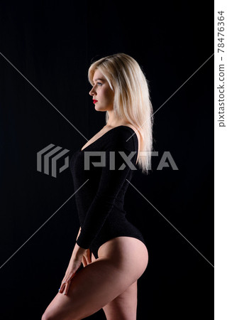 Young blonde plump woman with bright makeup in black bodysuit at dark background 78476364