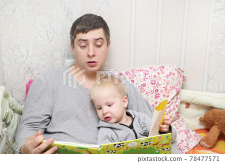 Dad reads his son a bedtime story 78477571