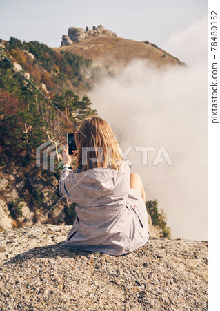 Woman is sitting on the stones, resting, taking photo and enjoying the view and the fresh air. 78480152