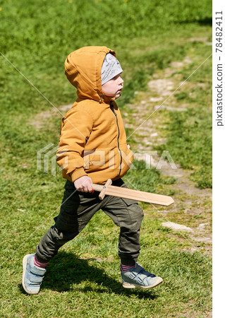 A child in a jacket and a hat with a wooden sword in his hands plays outdoors A child in a jacket and a hat with a wooden sword in his hands plays outdoors 78482411