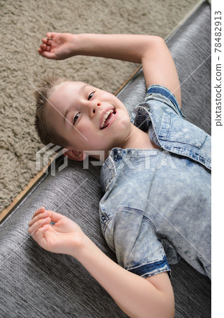 Cute funny boy lying upside down on sofa looking at camera, smiling playful child boy having fun at home. 78482913