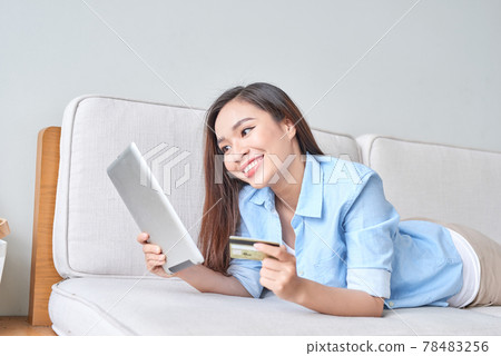 happy woman using digital tablet for online shopping with credit card in the living room 78483256