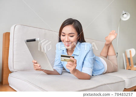 happy woman using digital tablet for online shopping with credit card in the living room happy woman using digital tablet for online shopping with credit card in the living room 78483257