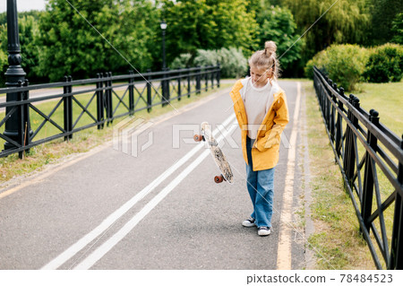 Happy teenage girl learning to ride a skateboard in the city park. 78484523