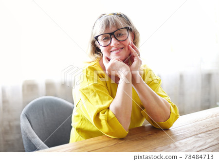 Happy middle aged woman sitting at table 78484713