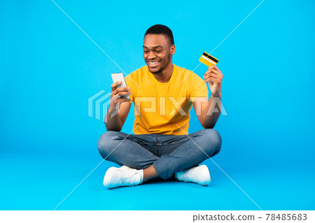 African Man Holding Credit Card And Smartphone Over Blue Background African Man Holding Credit Card And Smartphone Over Blue Background 78485683