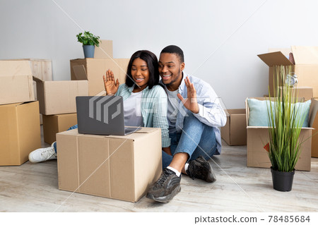 Young black family chatting online via laptop, sitting among carton boxes in new apartment and waving hands to camera Young black family chatting online via laptop, sitting among carton boxes in new apartment and waving hands to camera 78485684