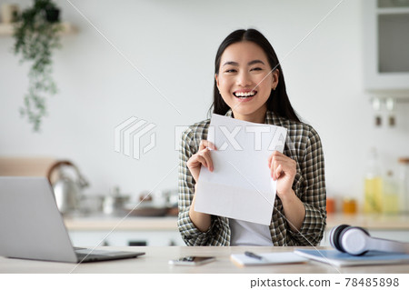 Cheerful asian woman showing empty paper, kitchen interior Cheerful asian woman showing empty paper, kitchen interior 78485898