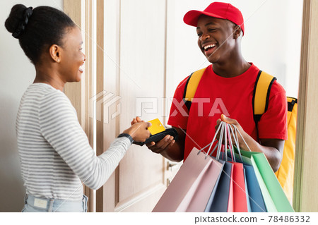 Cheerful Black Woman Paying Courier Using Credit Card At Home 78486332