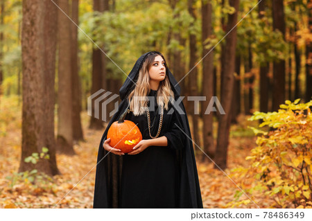 Young witch with jack o lantern in forest Young witch with jack o lantern in forest 78486349