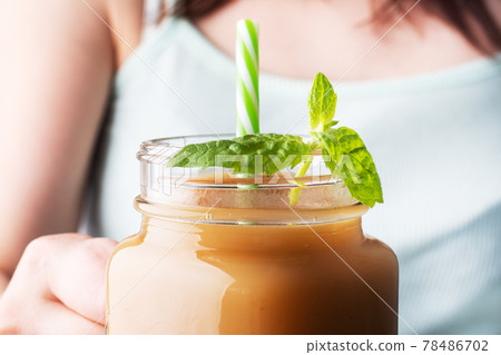A young girl holds a glass mug with juice in her hand. Fresh juice with mint. Selective focus. 78486702