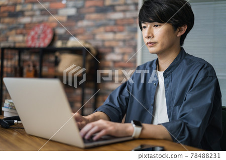 A man in his early twenties working on a laptop 78488231