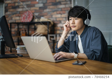 A man in his early twenties wearing headphones working on a laptop 78488254