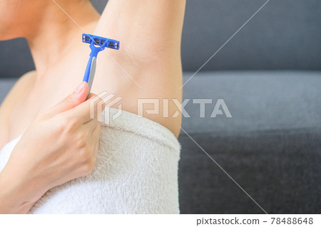 Young woman shaving armpit with blue shaver on blur background. Closeup of a girl hand with a razor shaving armpit. Armpit epilation hair removal. Depilation and skin care concept. 78488648