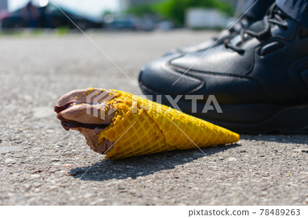 A man threw a tasteless chocolate ice cream in a waffle cone on the asphalt under his feet, taking a bite 78489263