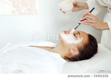 Crop cosmetologist applying facial mask on client 78491836