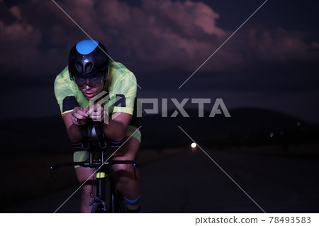 triathlon athlete riding bike fast at night 78493583