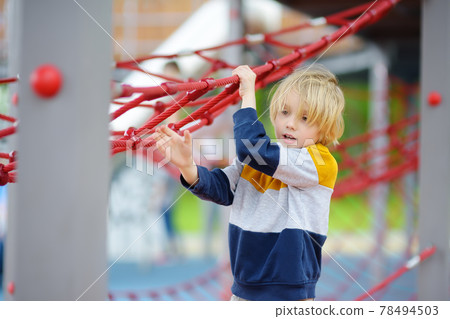 Cute preschooler boy having fun on outdoor playground. Spring/summer/autumn active sport leisure for kids. Activity for children. Equipment of entertainment park for kids. Cute preschooler boy having fun on outdoor playground. Spring/summer/autumn active sport leisure for kids. Activity for children. Equipment of entertainment park for kids. 78494503