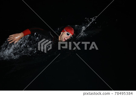 triathlon athlete swimming in dark night wearing wetsuit 78495384