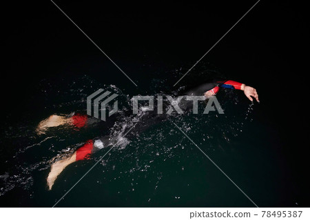 triathlon athlete swimming in dark night wearing wetsuit 78495387