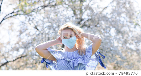 A girl in protective medical mask in spring among the blooming garden. Spring allergy conception 78495776