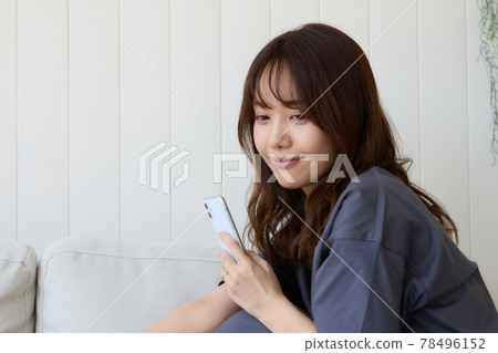 一個女人在客廳裡看著她的智能手機 一個女人在客廳裡看著她的智能手機 78496152