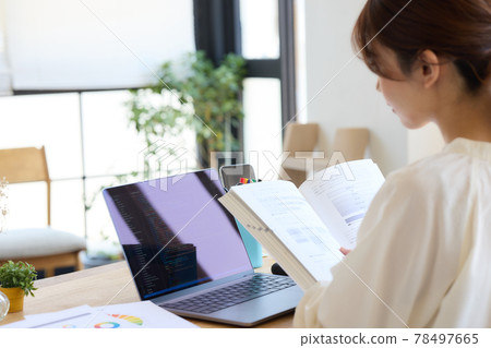 A woman studying while looking at a reference book at her desk 78497665