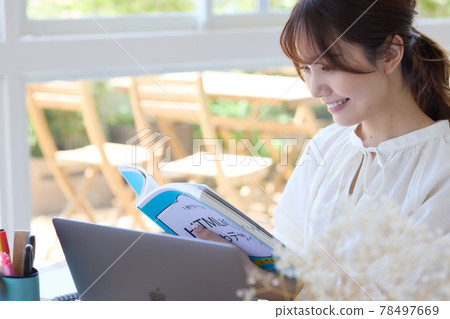 一位女士一邊在辦公桌前看參考書一邊學習 78497669