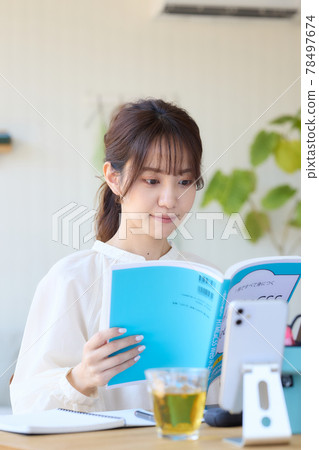 A woman studying while looking at a reference book at her desk 78497674