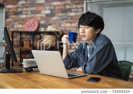 A man in his twenties looking at a laptop screen with a mug A man in his twenties looking at a laptop screen with a mug 78498484