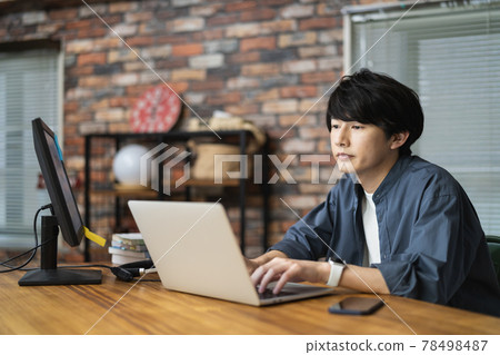 A man in his early twenties working on a laptop 78498487