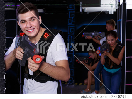 Excited guy holding laser pistol, playing laser tag with friends in dark room Excited guy holding laser pistol, playing laser tag with friends in dark room 78502913