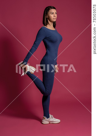 Young woman stretching leg muscles on maroon background 78503078
