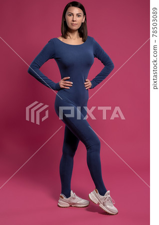 Woman confidently standing in yoga jumpsuit on maroon background 78503089