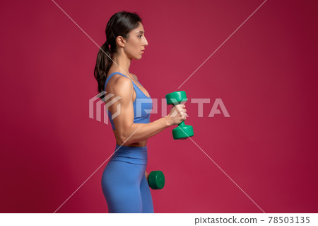 Girl performing arm exercises with dumbbells on maroon background Girl performing arm exercises with dumbbells on maroon background 78503135