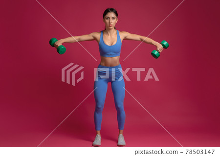 Girl performing dumbbell lateral raise on maroon background 78503147