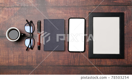 Mock up mobile phone, empty frame glasses, notebook and coffee cup on wooden background. 78503254