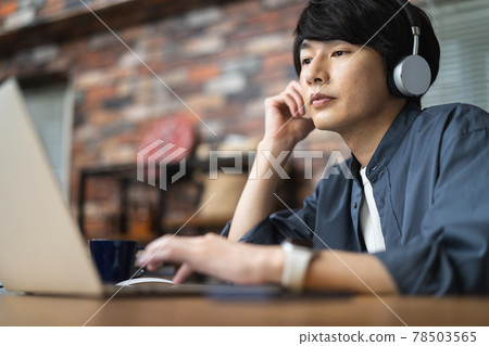 A young man with headphones working on a laptop A young man with headphones working on a laptop 78503565