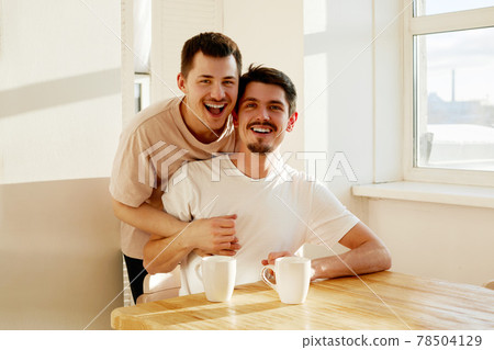 Happy gay couple enjoying hot beverage at home Happy gay couple enjoying hot beverage at home 78504129