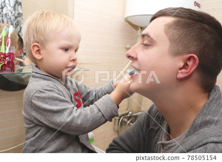 Dad and son brush their teeth in the bathroom. Father Brushing Teeth to Child 78505154