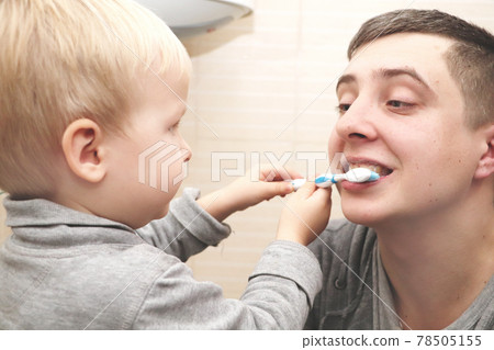 Dad and son brush their teeth in the bathroom. Father Brushing Teeth to Child Dad and son brush their teeth in the bathroom. Father Brushing Teeth to Child 78505155