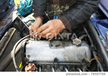 The car mechanic unlocks the motor cover of an old car and will repair it. The car mechanic unlocks the motor cover of an old car and will repair it. 78507788