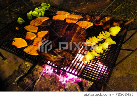 A charcoal barbecue at night, grilling steaks and vegetables 78508485