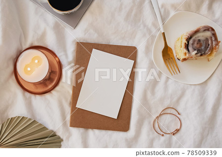 Paper card mock-up on the bed with coffee, candle and cinnamon roll Paper card mock-up on the bed with coffee, candle and cinnamon roll 78509339