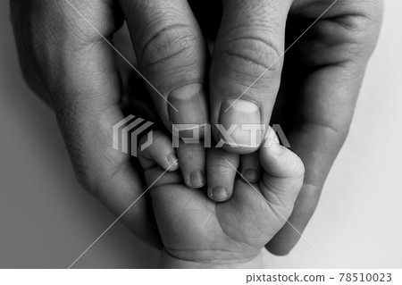 A newborn holds on to mom's, dad's finger. Hands of parents and baby close up. A child trusts and holds her tight. Black and white photo. A newborn holds on to mom's, dad's finger. Hands of parents and baby close up. A child trusts and holds her tight. Black and white photo. 78510023
