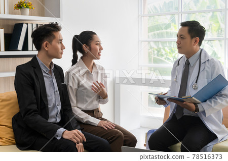 A young Asian couple is consulting with a doctor about pregnancy planning.The doctor is reporting the health check-up to the couple and explaining the treatment guidelines, taking care of the health. 78516373