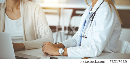 Unknown woman-doctor communicating with female patient in sunny clinic. Physician checks medical history record and exam results, close-up Unknown woman-doctor communicating with female patient in sunny clinic. Physician checks medical history record and exam results, close-up 78517689