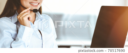 Brunette female customer service representative using headset and consulting clients online. Call center Brunette female customer service representative using headset and consulting clients online. Call center 78517690
